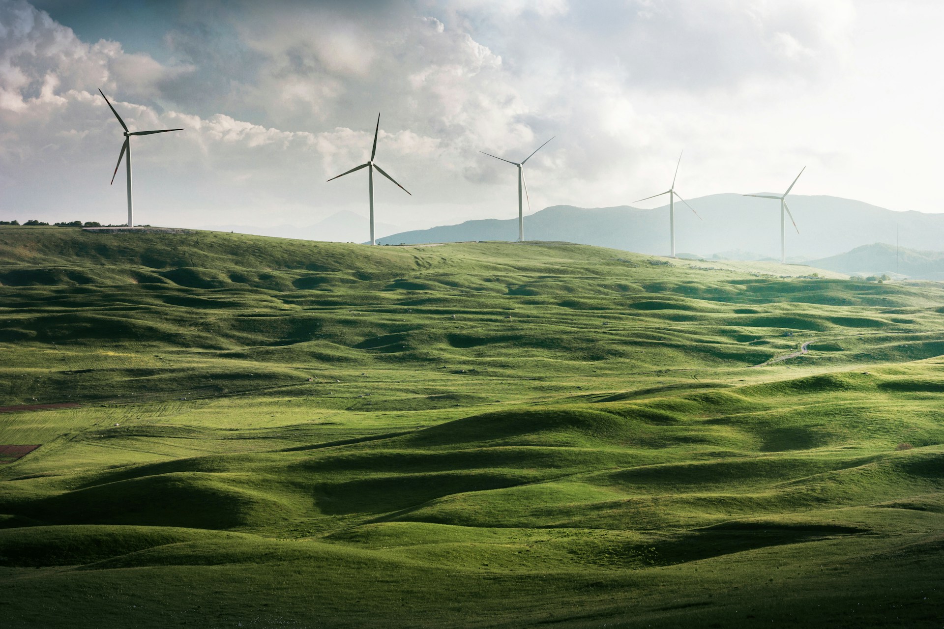 Yeşil tepeler üzerinde elektrik üreten rüzgâr türbinleri