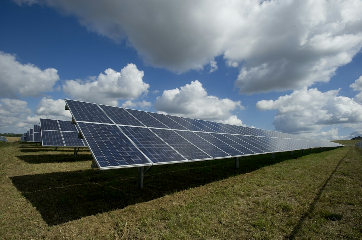 Bulutlu mavi gökyüzünün altında yenilenebilir enerji üreten güneş panelleri